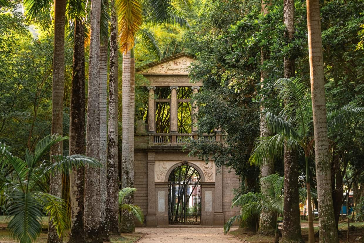 Historisches steinernes Tor mit S&auml;ulen, umgeben von hohen Palmen und dichter Vegetation im Botanischen Garten