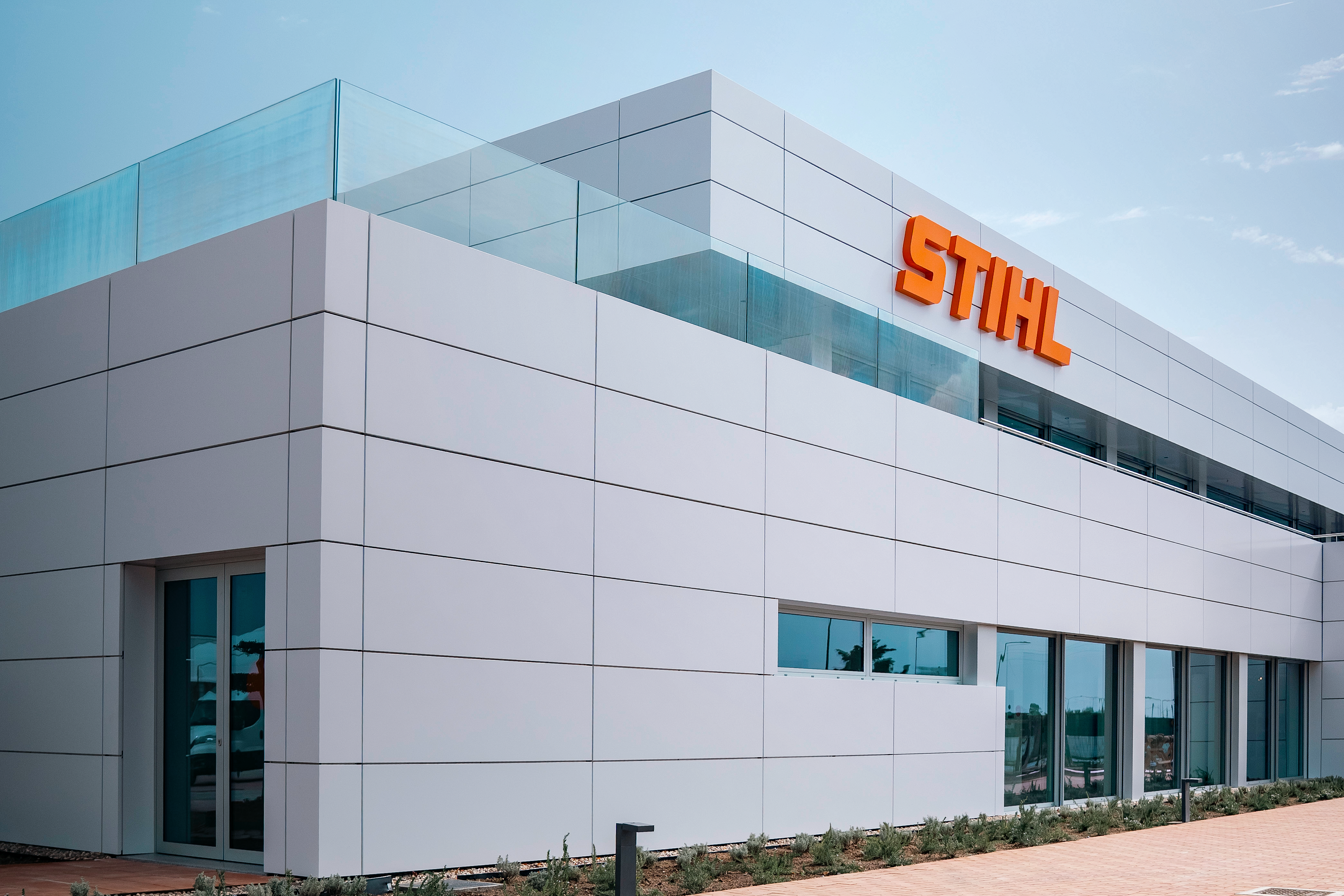 Moderner STIHL Bau mit wei&szlig;er, klar gegliederter Fassade, Glasfronten und orangefarbenem Logo unter blauem Himmel.