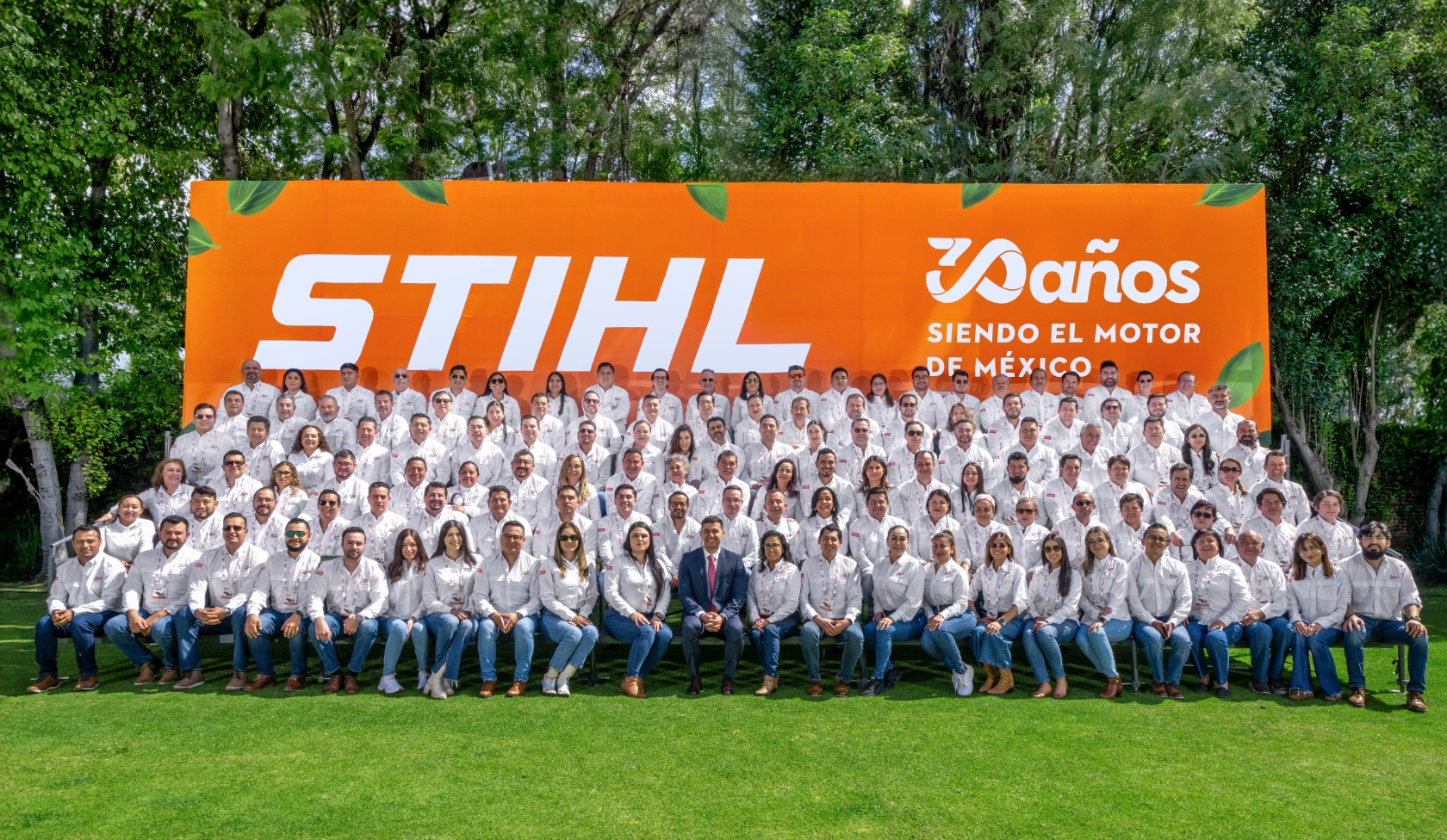 Gro&szlig;e STIHL Belegschaft vor orange Jubil&auml;umstafel zu 30 Jahren in Mexiko, alle in wei&szlig;en Hemden, Gruppenfoto auf Rasen