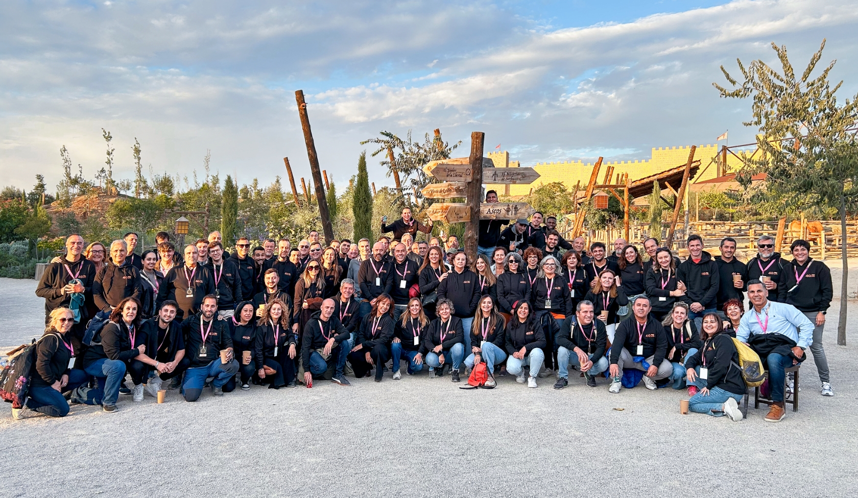 Gro&szlig;e STIHL Gruppe in schwarzen Hoodies posiert auf Platz mit B&auml;umen und Holzelementen, gemeinsame Teamreise im Abendlicht