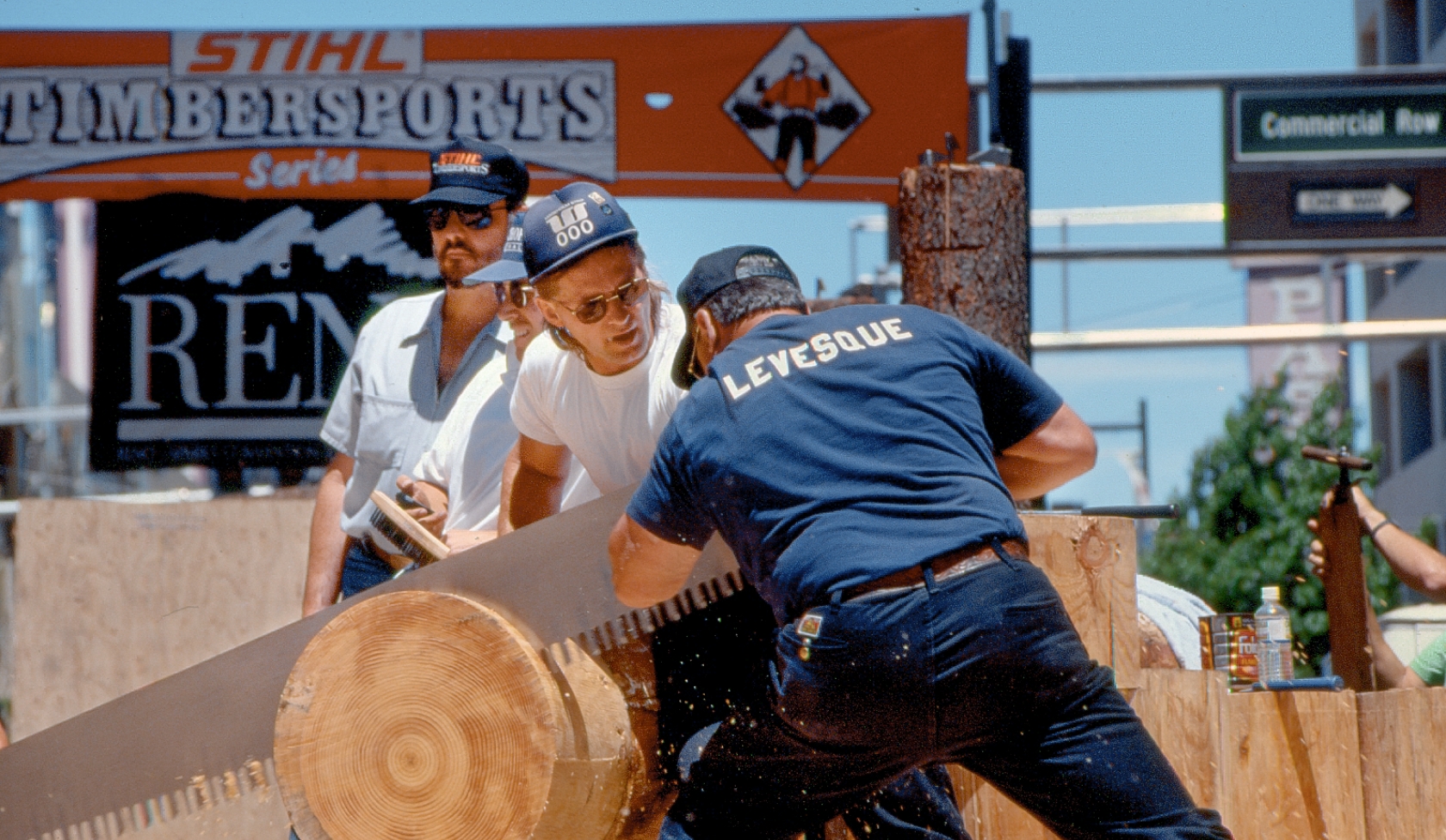 Fr&uuml;he STIHL Timbersports Szene mit Athleten, die an gro&szlig;em Stamm mit Zweimanns&auml;ge arbeiten, Zuschauer nah am Wettkampftisch