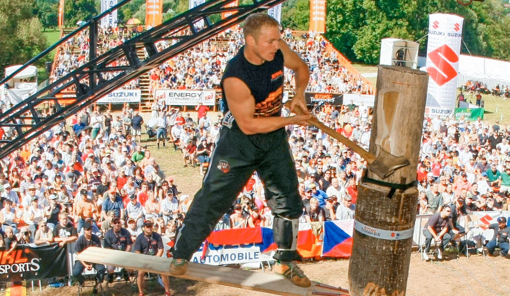 Athlet steht auf Brett im Stamm und schl&auml;gt mit Axt beim STIHL Timbersports Wettkampf, gro&szlig;e Trib&uuml;ne voll jubelnder Fans