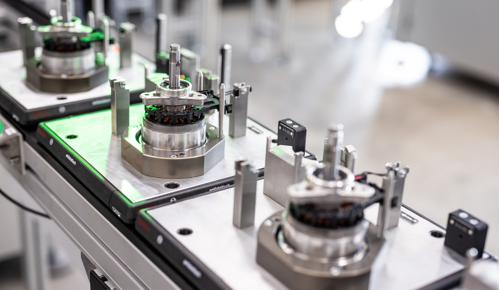 Montageplatz mit mehreren eingespannten Elektromotoren, Metallgeh&auml;use und Sensoren, gr&uuml;n beleuchtete Pr&uuml;ffl&auml;che im Vordergrund