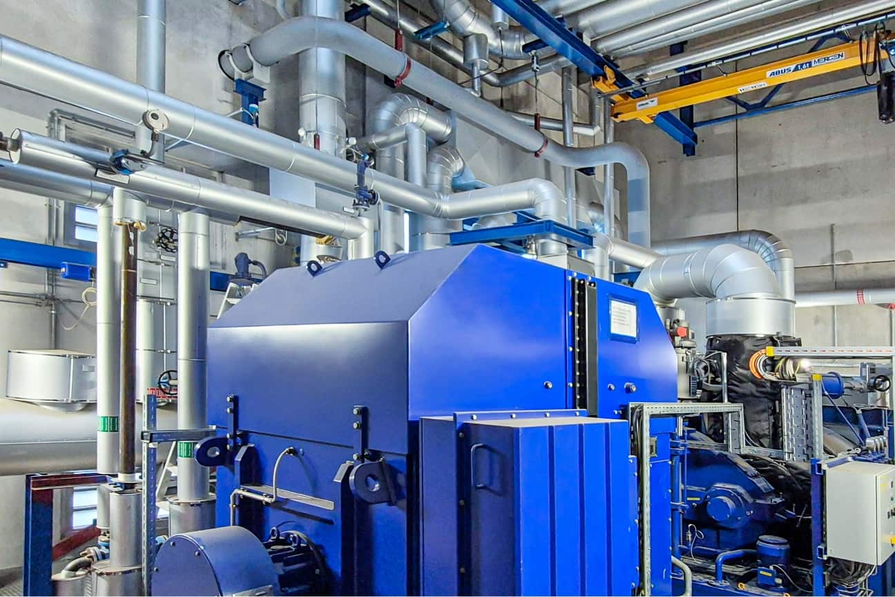 Innenansicht technischer Anlage mit gro&szlig;em blauen Aggregat, vielen silbernen Rohrleitungen und Energietechnik im Industriebau